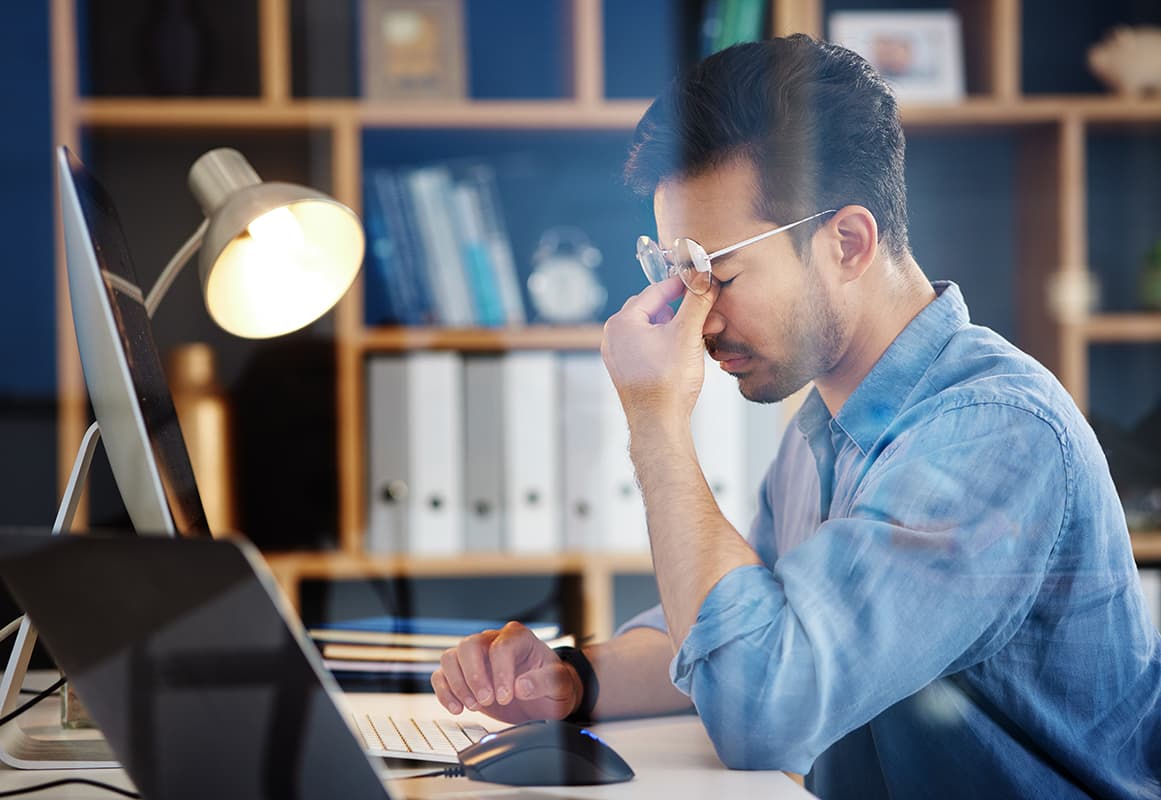 Stressed office worker with eyestrain using computer at workplace.