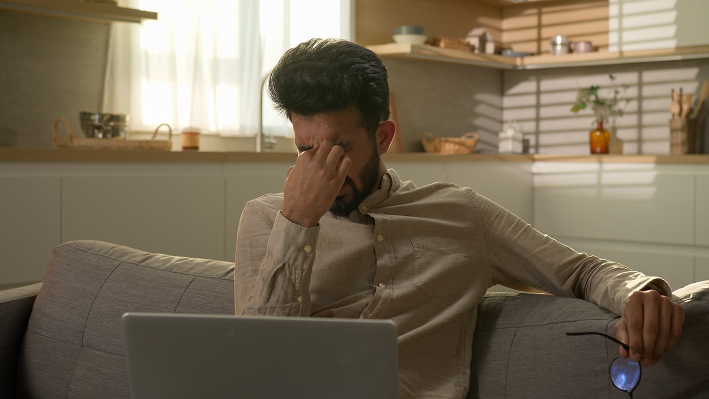 Exhausted man working from home, symbolizing work-related stress. 